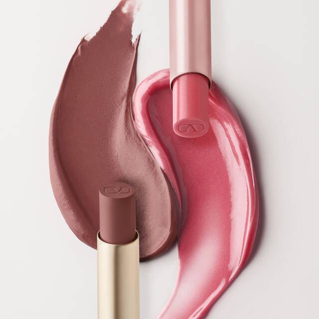 Ein geteiltes Bild, das Kosmetikprodukte zeigt. Auf der linken Seite sind zwei Farbfelder von rosa Lippenprodukten sichtbar, eines in einem helleren braunlich-rosa und das andere in einem helleren, glanzenden Rosa. Ein Valentino Spike Lippenbalsam-Tube und ein Lipgloss-Tube sind daneben positioniert. Die rechte Seite zeigt eine verpackte Spike Valentino Disco Balm und eine verpackte Spike Valentino Matte, mit ihren entsprechenden Farbmustern darunter.