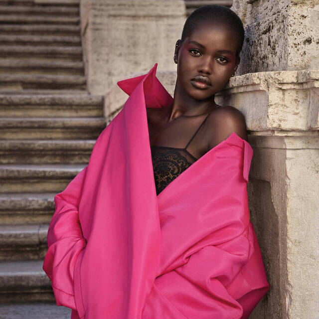 Ein Modell mit kurzem Haar tragt einen pinken Mantel uber einem schwarzen Tops und posiert an einer Treppe.
